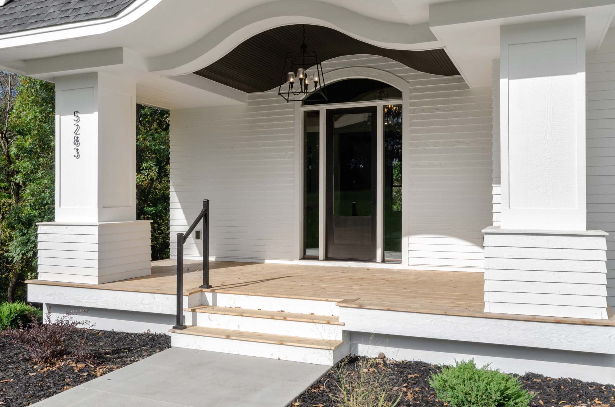 Close up of modern white farmhouse with black front door and large cedar porch.