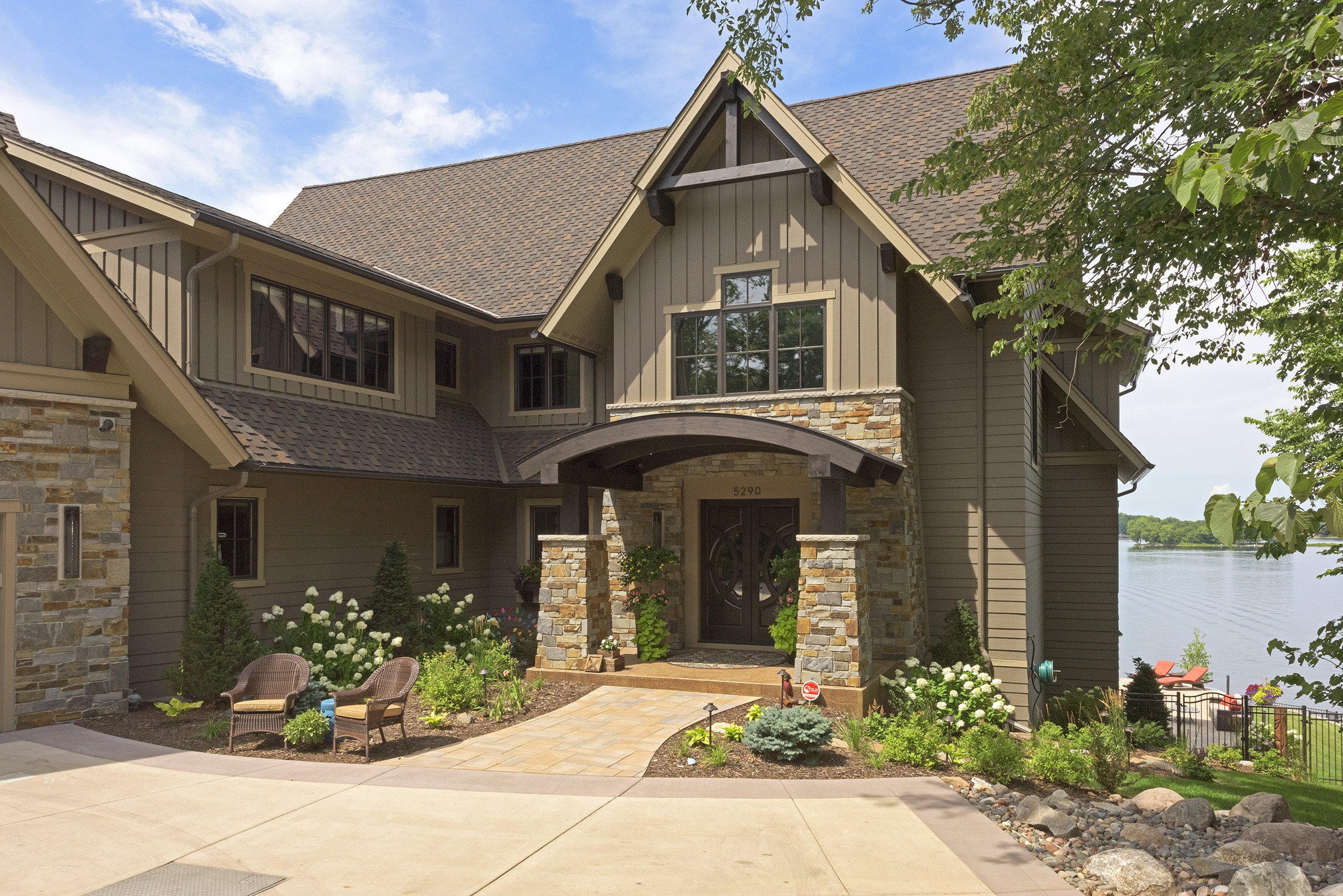 Large brown home on a lake with grand front door with stone surround.