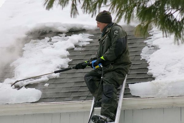 Man on ladder removing ice dams on roof.