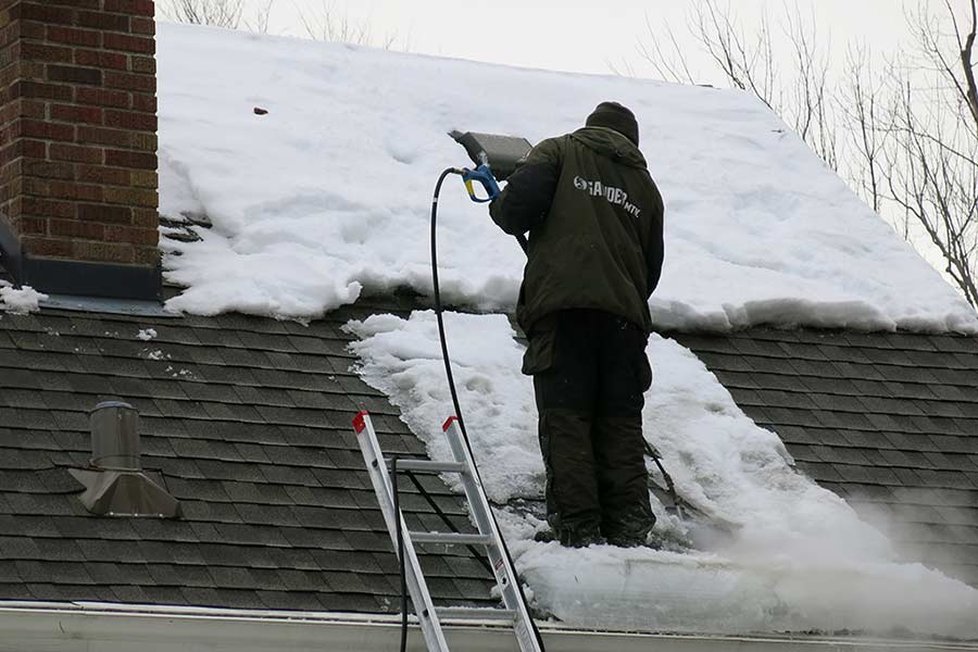 Man on shingled roof removing an ice dam.