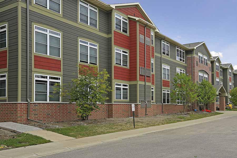 Three story commercial apartment building with green and bright red siding and red brick accents.