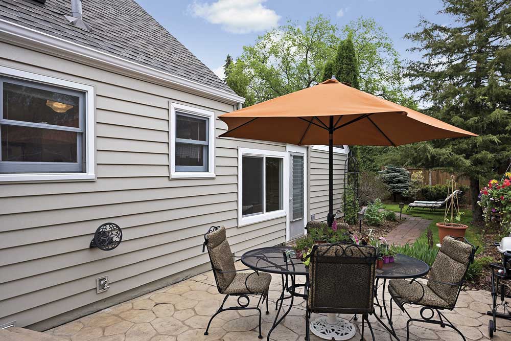 Tan single story home with nice stone patio and outdoor dining furniture.