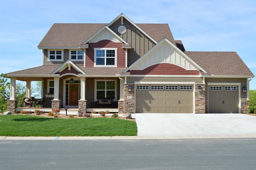 Light brown and red two story home with large wrap around porch with stone trim.