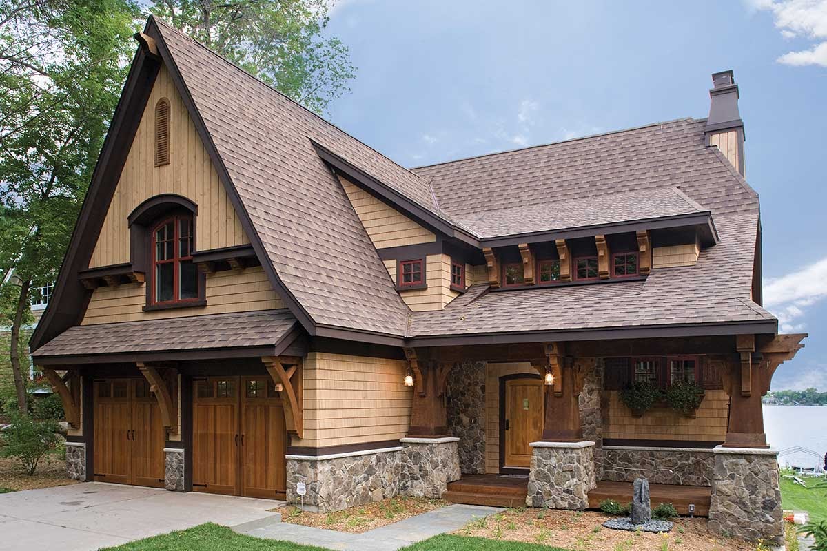 Rustic wood home on a lake with steep garage gable and nice stone accents.