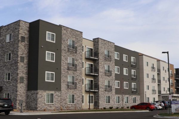 Long four story commercial apartment building with deep green siding and stone accents.