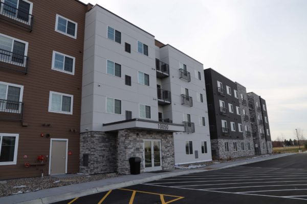 Exteriors by Highmark four story commercial apartment building with white and rust colored siding and stone trim.