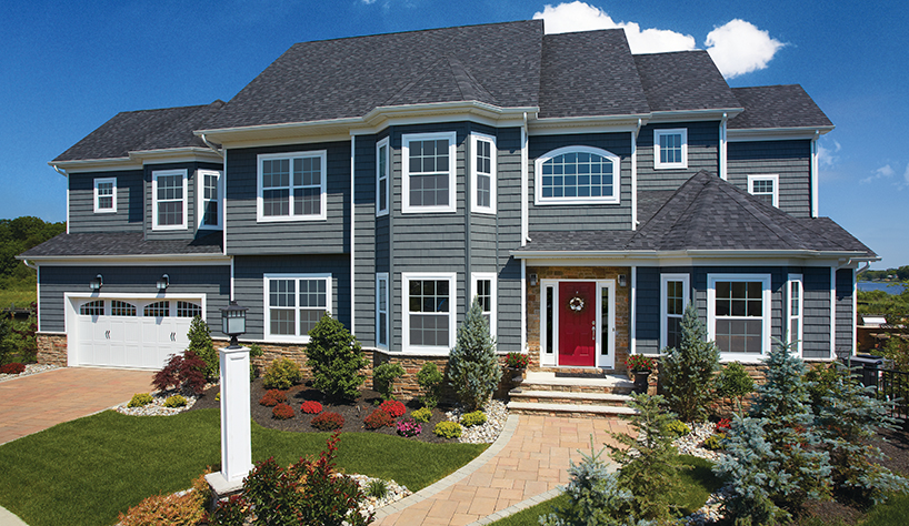 Big blue-gray two story home with red front door and immaculate landscaping.