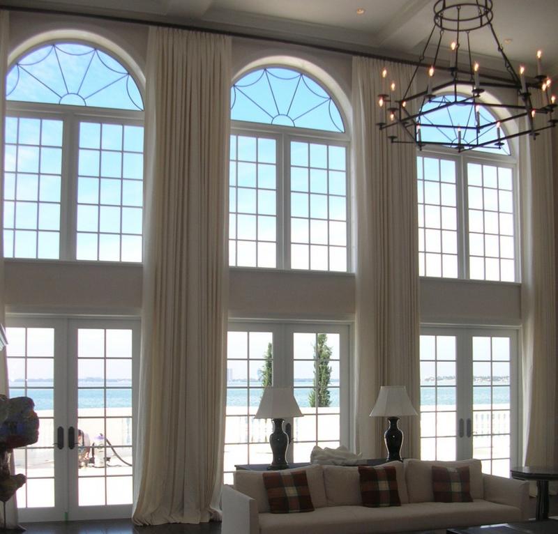 Inside a massive living room with floor to ceiling windows and drapes and cool chandelier.