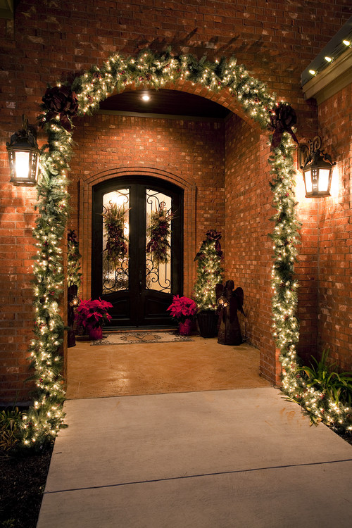 Grand front door entryway at night on brick home with christmas lights and garland.