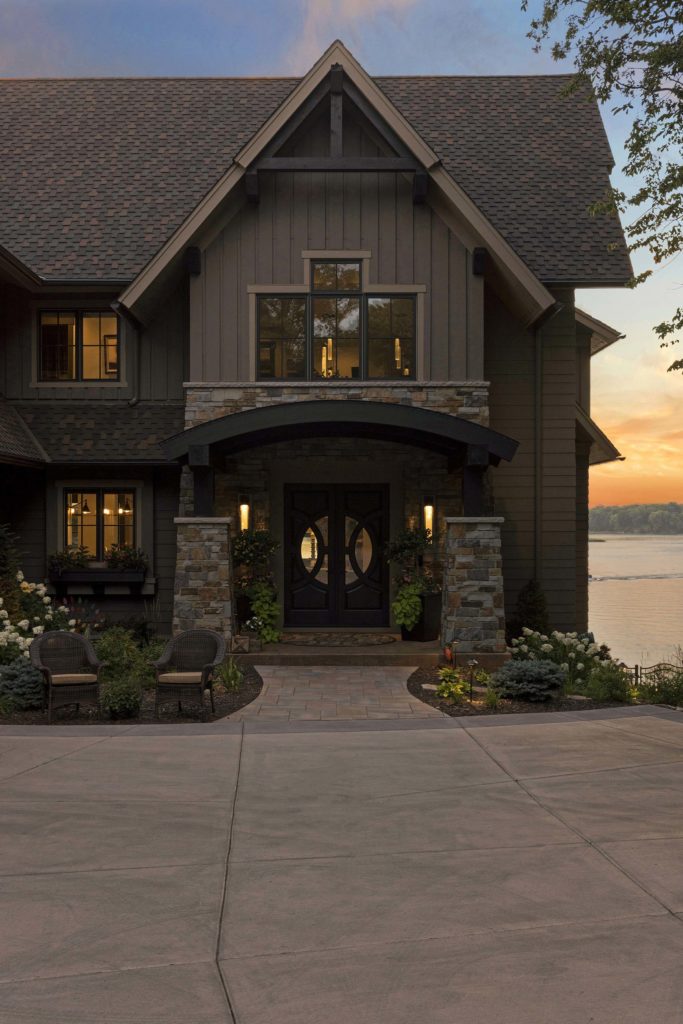 Dark brown two story lake home with large gable front door and stamped concrete driveway.