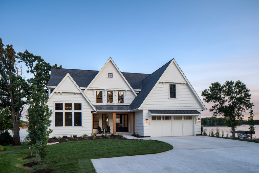 A white house with a large garage and a lake in the background offers a serene and picturesque setting for those looking to get a free roofing inspection in Minnesota.