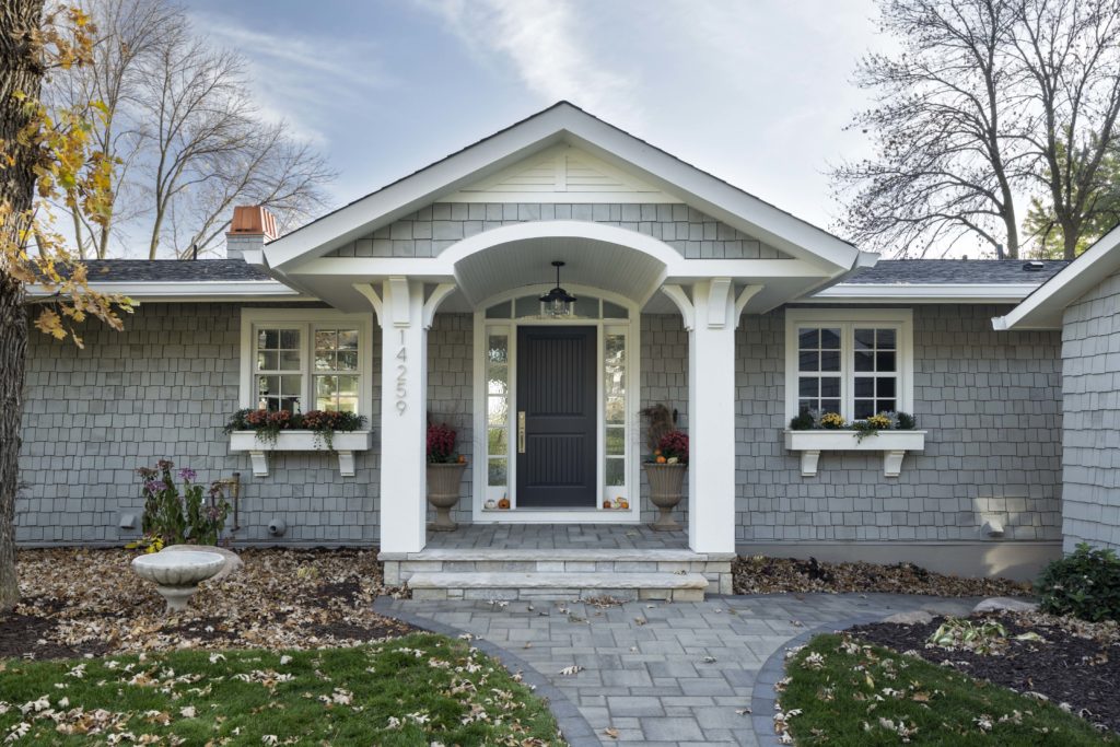 Grey rambler style home with shake siding and leaves on the ground surrounding the home