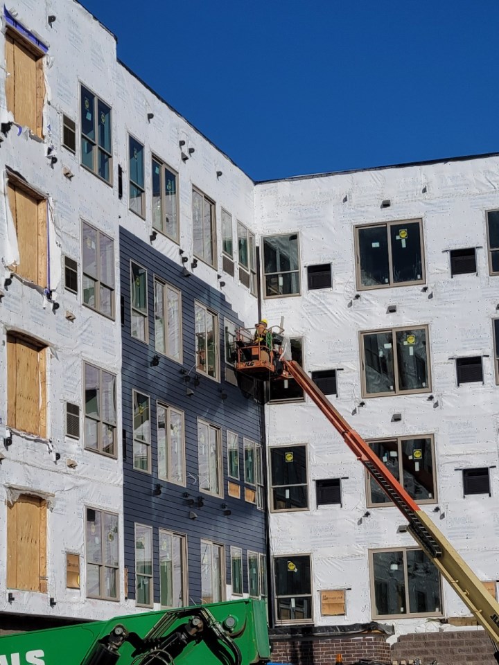 A five-story apartment building with siding being installed by Exteriors by Highmark worker.