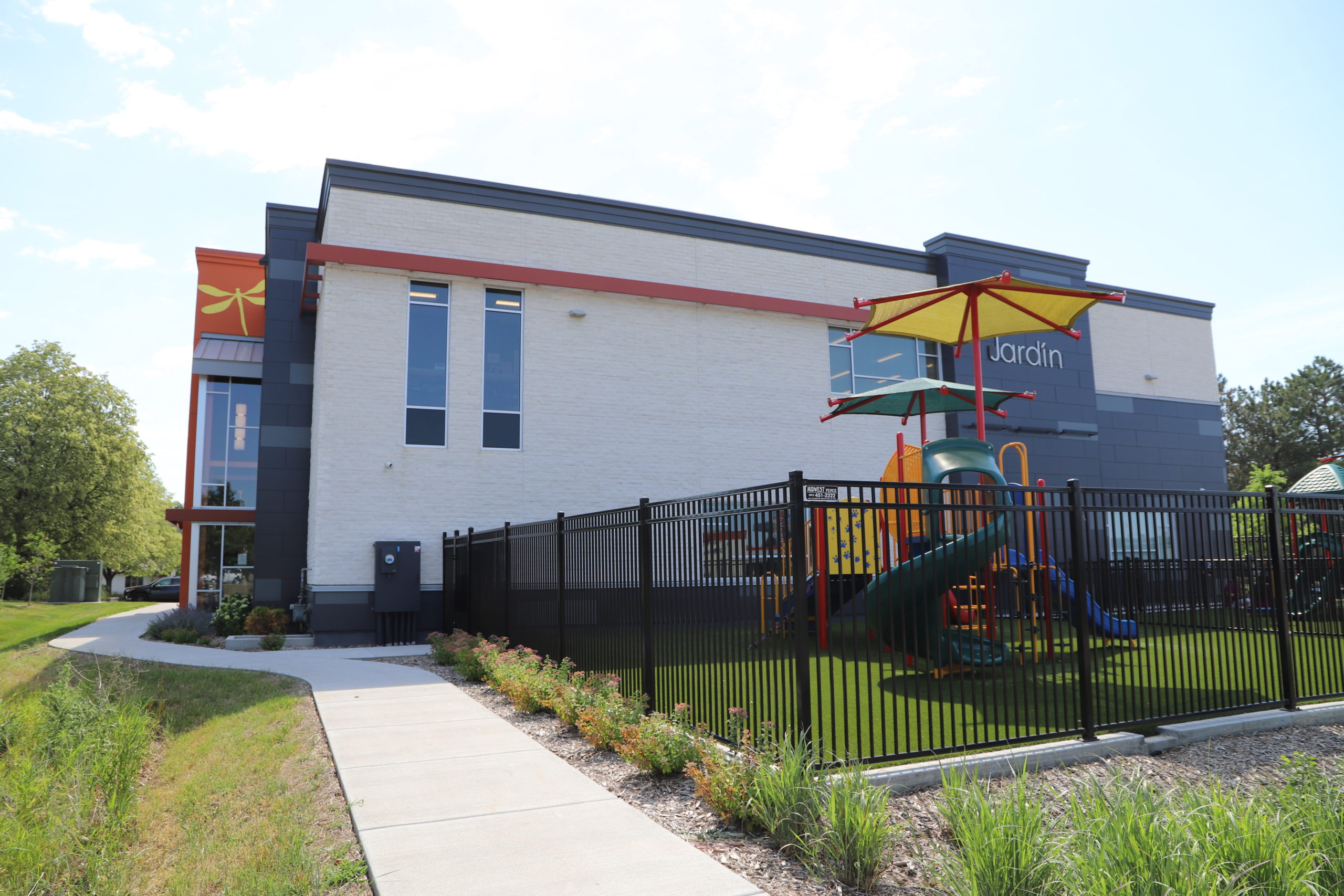 Large multi colored commercial building with a fenced area in front containing playground equipment.