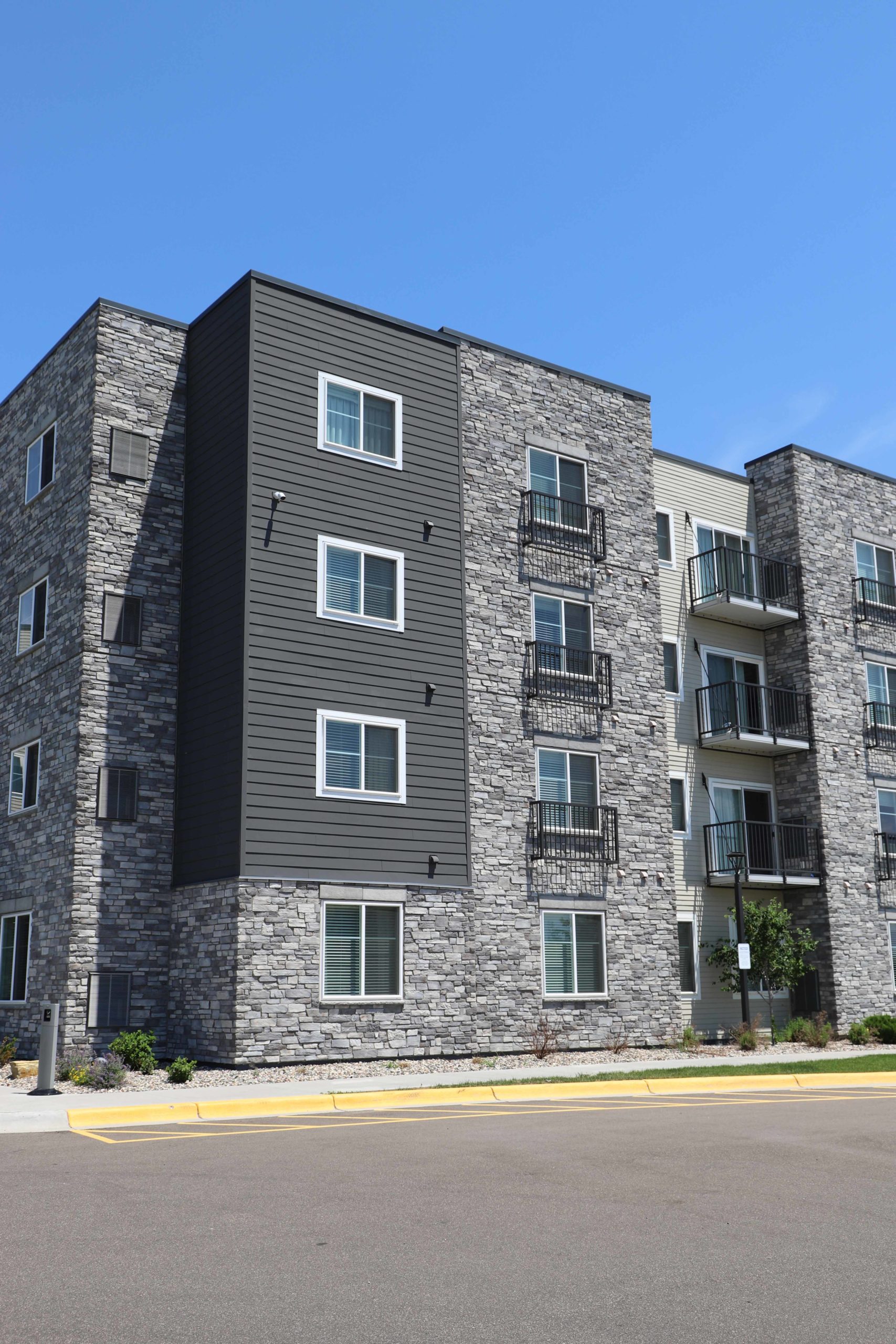 The corner of a four-story apartment building with a dark gray James Hardie Lap siding and stone exterior in Plymouth, MN.