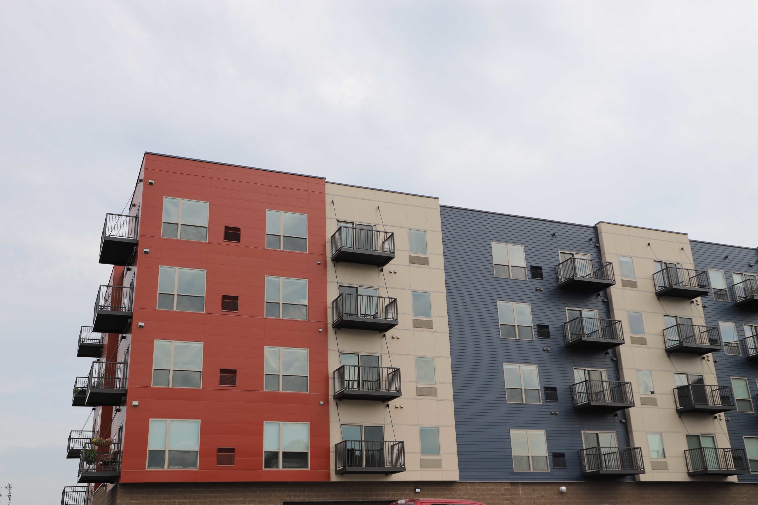 A red, cream and blue five-story apartment building with balconies in Shakopee, MN.