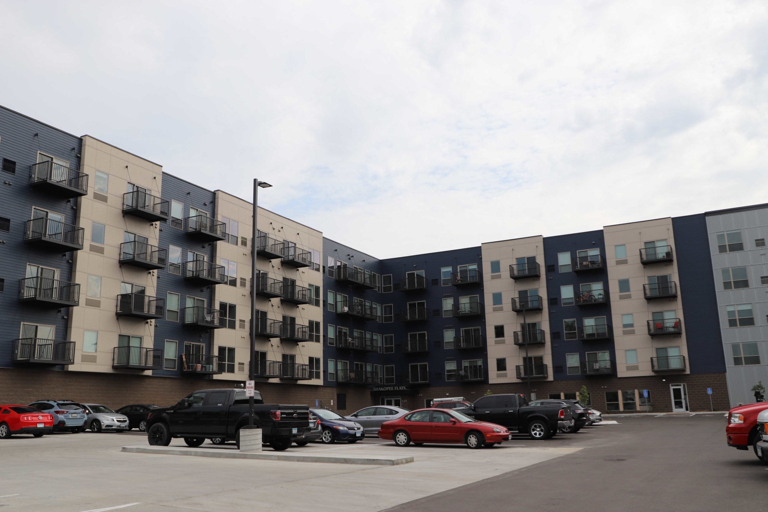 Blue and cream colored, L-shaped five-story apartment building and parking lot in Shakopee, MN.