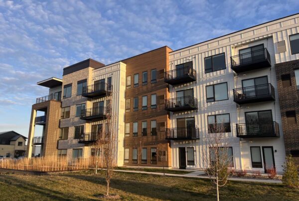 OMRY Apartments offer a contemporary living experience with diverse exterior finishes, inviting balconies, and a beautifully landscaped lawn under a partly cloudy sky.