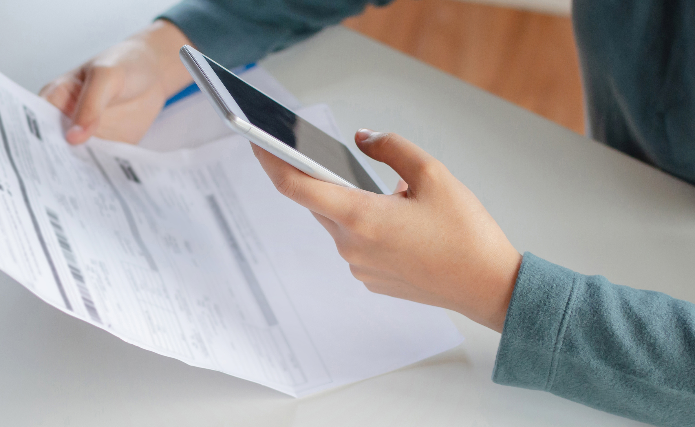 A person holds a smartphone in one hand and a document detailing the top signs of a bad roof in the other, appearing to take a photo or scan the document.